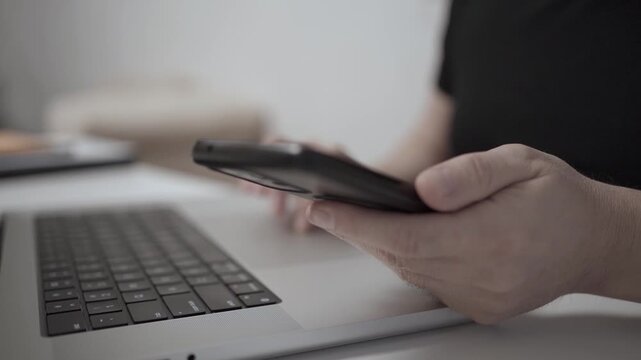 Multitasking Man Browsing Smartphone While Working on Laptop