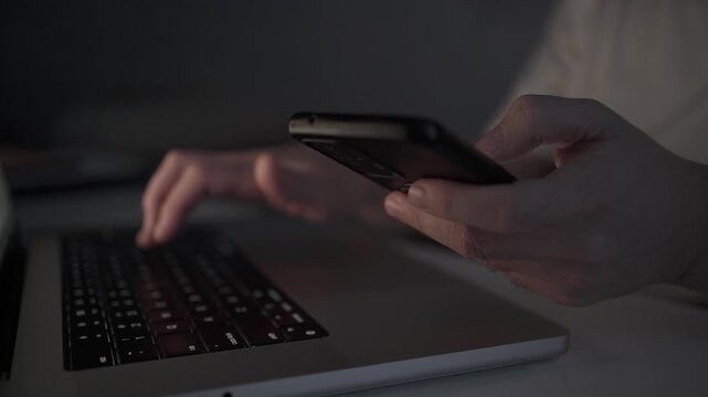 Multitasking Man Browsing Smartphone While Working on Laptop