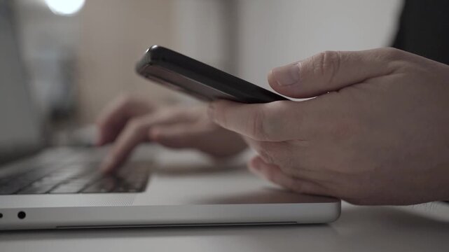 Multitasking Man Browsing Smartphone While Working on Laptop