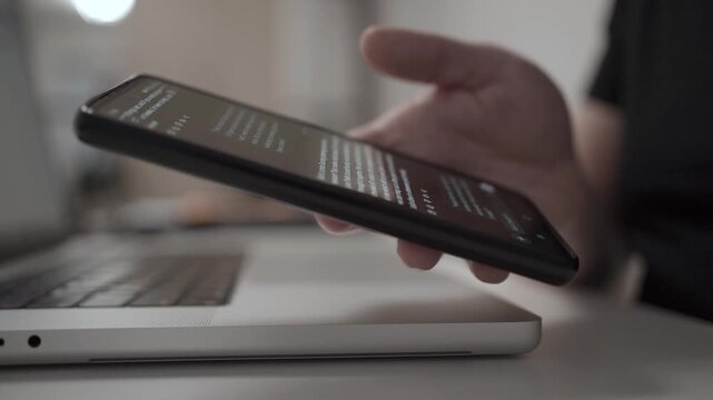 Multitasking Man Browsing Smartphone While Working on Laptop
