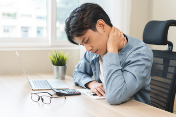 Body muscles stiff problem, ache asian young man pain neck and shoulder while sitting work on chair at home, male holding massaging rubbing, hurt or sore body. Healthcare people, office syndrome.
