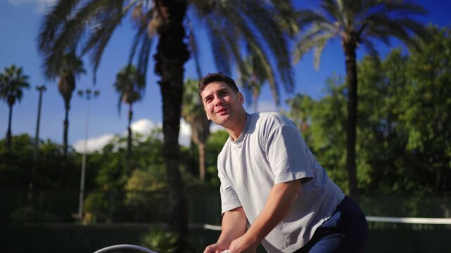 Athletic man executing strong backhand swing on outdoor tennis court, dynamic sport action under palm trees, bright sunlight, active lifestyle moment, focused training