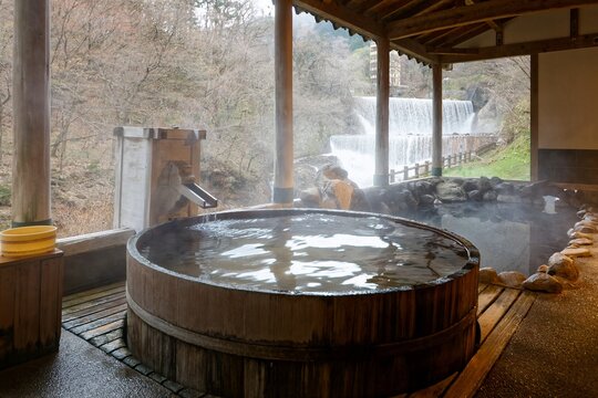 A serene vista at Tsuchiyu Onsen in Fukushima features a large, steaming cypress tub with an unobstructed view of a cascading two-tiered waterfall, a carefully integrated sabo dam along the Higashikar