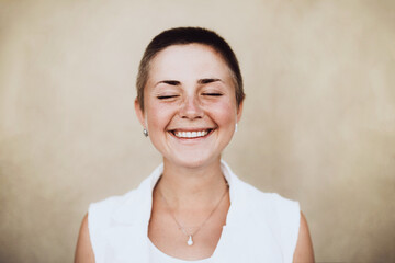 Young woman with a buzz cut smiling broadly with closed eyes, expressing pure joy and happiness,...