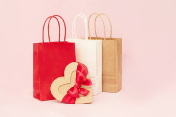 A holiday backdrop with a heart-shaped cardboard box with a bow, gift bags, on a pink background. Perfect for holiday shopping, Mother's Day, weddings, and Valentine's Day.
