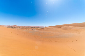 Sossusvlei in Namibia is an iconic Namib Desert landscape with towering red sand dunes, bright white clay pans, and ancient dead camel thorn trees beneath a deep blue sky. One of the oldest deserts on