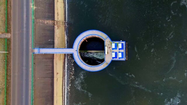 Circular hydraulic structure seen from drone cuts through frozen water surface creating strong geometric winter composition
