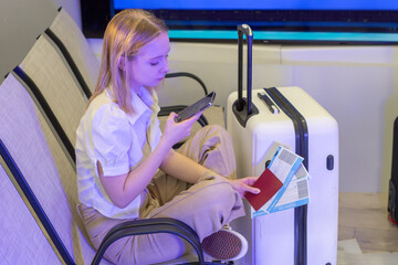 Traveler an airport waiting area with a smartphone, boarding passes and suitcase