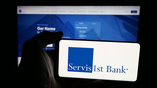 Stuttgart, Germany - 12-12-2025: Person holding mobile phone with logo of US bank ServisFirst Bancshares Inc. on screen in front of web page. Focus on phone display.