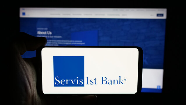 Stuttgart, Germany - 12-12-2025: Person holding cellphone with logo of US bank ServisFirst Bancshares Inc. on screen in front of webpage. Focus on phone display.