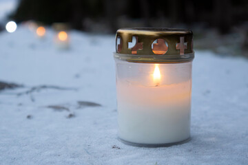 Selective focus on a row of lit memorial candles outside a cemetery, burning in memory of the dead.