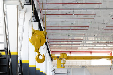 Industrial workshop with an overhead crane fire safety system red pipes. A bright yellow crane hook is suspended from the ceiling. Concept of industry, manufacturing, engineering, interior