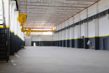 Industrial workshop with an overhead crane fire safety system red pipes. A bright yellow crane hook is suspended from the ceiling. Concept of industry, manufacturing, engineering, interior