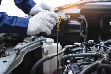 Close-up shot mechanician checking engine lubricant oil level at auto service station.