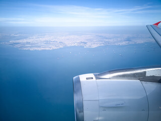 View from passenger airplane window showing jet engine above deep blue sea with distant coastline on horizon. Plane flying bye Istanbul