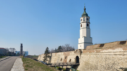 View of historic fortress with tall clock tower and massive stone walls under clear blue sky. Sahat Tower of Kalemegdan fortress, Belgrade, Serbia