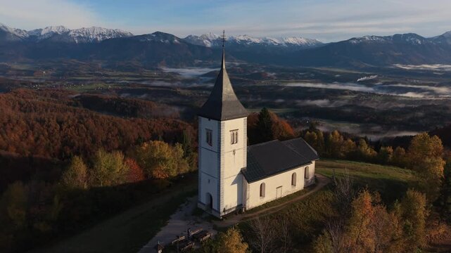 Majestic aerial view of the Church of Saint Primus and Felician on a hilltop during a foggy sunrise. Slovenia.
