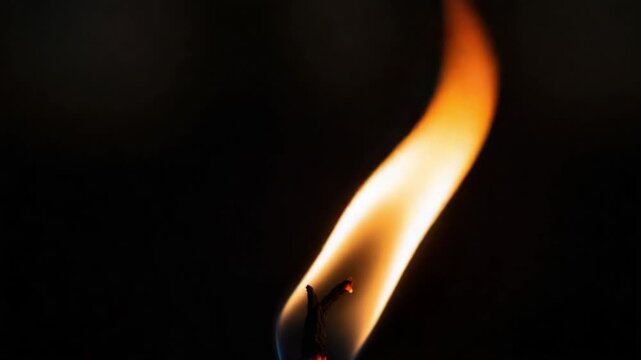 A closeup view of a candle flame burning brightly in darkness