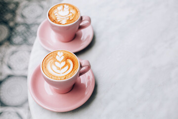 Two beautiful pink cups of cappuccino with latte art on the table.