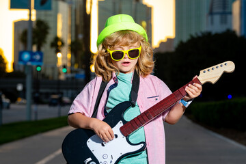 Cool kid playing guitar outdoors. Stylish child with electric guitar. Young musician performing in...