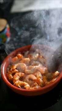 Vertical gourmet shrimp and prawns cooking in olive oil stirred with wooden spoon in clay pot, Spanish recipe for prawns in pil pil sauce