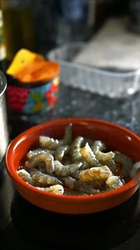 Preparation of a recipe for prawns and langoustines in pil pil sauce with fried garlic, olive oil and hot chili peppers, vertical view, cooking scene with clay pot, Spanish garlic recipe