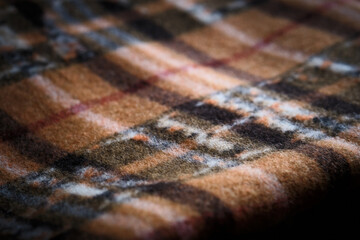 Macro close-up of brown plaid fabric showing woven texture and intersecting lines. Textile pattern, softness, and material detail