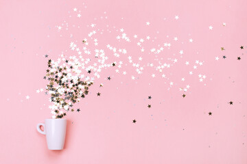 White cup jug with little star-shaped sparkles, pouring out of it. Flat lay.