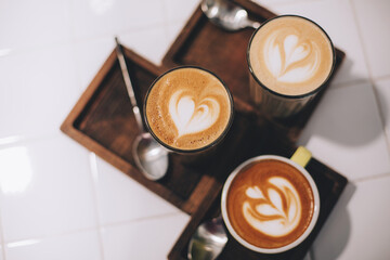 Tree cups of coffee with beautiful latte art and spoons on wooden boards, on white background.