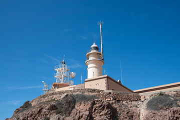 The Cabo de Gata lighthouse, Almeria, Spain, stands on a rocky cliff under a clear blue sky. 