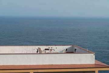 Rooftop terrace with plastic chairs and a table facing the Atlantic Ocean in Puerto de la Cruz, Tenerife, Spain. A peaceful, minimal seaside scene with endless blue horizon
