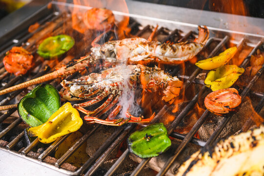 Grilled spiny lobsters with flames, pineapple and vegetables on an open outdoor grill