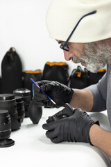 A professional photographer wearing gloves and a beanie carefully cleans a camera sensor using a specialized swab. A detailed shot focused on precision and gear maintenance.