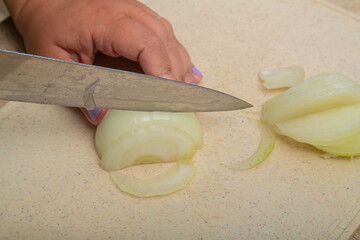 Sweet white onion is cut with a knife on a wooden board on the table