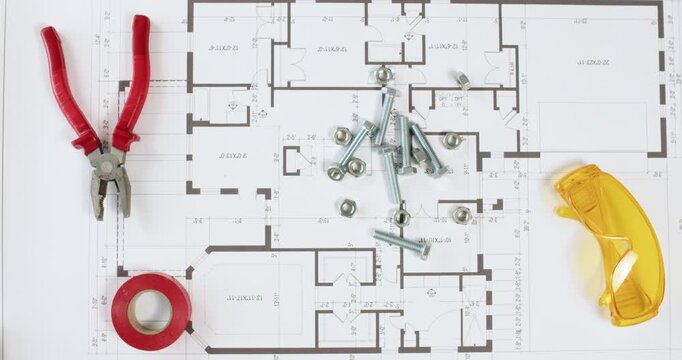 A worker pours a set of metal bolts and nuts onto a paper plan of a house with his hands; construction supplies are lying on the plan.
