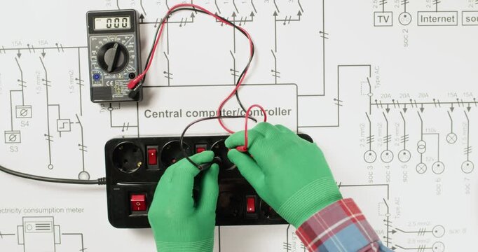 An electrician measures the current in the sockets of an extension cord, which is located on a paper plan of the house's electrical network.