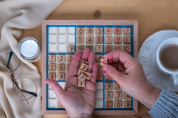 female hands placing number into Sudoku puzzle, solving puzzle on wooden board, brain workout, cognitive health, focus game, mental wellness
