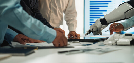 A modern office scene showing a collaboration between human hands and a robotic arm during a business meeting focused on technology and data analysis.Noogenesis