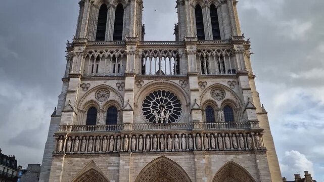 The Notre-Dame Cathedral facade in Paris, France, highlighting the intricate portals, the Gallery of Kings, the iconic rose window and two massive bell towers against a dramatic sky