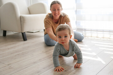 Mom assisting her baby in learning to crawl. Copy space, background.