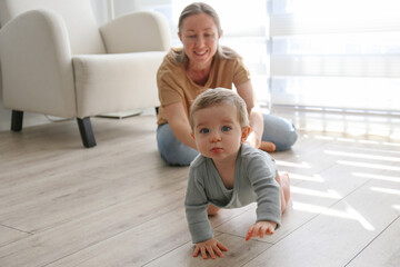 Mom assisting her baby in learning to crawl. Copy space, background.