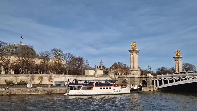View from a cruising boat trip along the Seine river to the breathtaking Pont Alexandre III in Paris, France. The bridge is adorned with gilded statues. The Grand Palais with glass dome in background