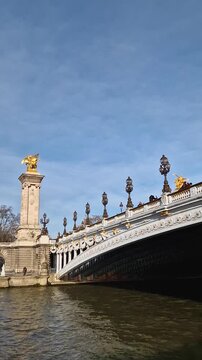 View from a cruising boat trip along the Seine river to the breathtaking Pont Alexandre III in Paris, France. The bridge is adorned with gilded statues. The Grand Palais with glass dome in background
