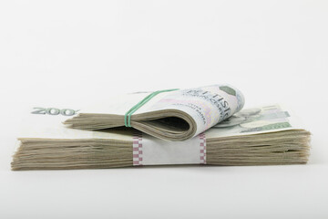 Two stacks of Czech Koruna banknotes are presented against a white backdrop in a still life photographed, Czech Republic, with one stack secured by a green rubber band and the other by a paper band.