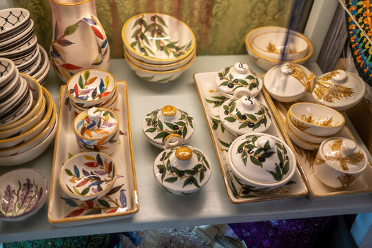 A set of handmade ceramic tableware including bowls and covered dishes with olive and wheat patterns on a shop shelf.