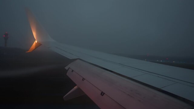 Commercial airplane wing view landing on night runway. Flaps and air brake spoilers deploy upon touchdown while condensation vortices form off the wing in foggy weather conditions.