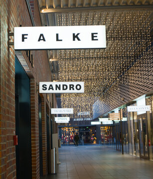 Passage adorned with decorative string lights and shops including Falke and Sandro in a shopping outlet. Outletcity Metzingen