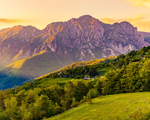 Vertical view of mountains in Sutjeska National Park at golden hour, warm sunset light over forested slopes and green meadows, peaceful wilderness landscape in Bosnia and Herzegovina, travel backgroun