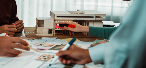 A group of architects collaborates in a modern workspace, examining sketches and a model. Colorful markers and design papers showcase the creative brainstorming process. SACTR