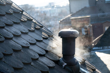 Rauch steigt aus einem kleinen Schornstein eines Hausdachs © Kostas Koufogiorgos
